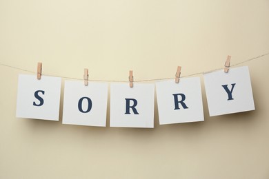 Word Sorry made of paper notes with letters hanging on rope against beige background