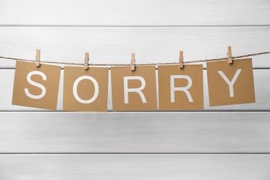 Word Sorry made of paper notes with letters hanging on rope against white wooden background