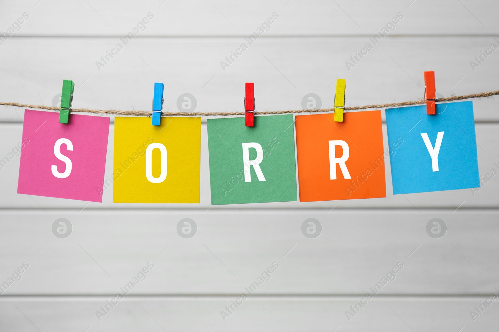 Image of Word Sorry made of paper notes with letters hanging on rope against white wooden background