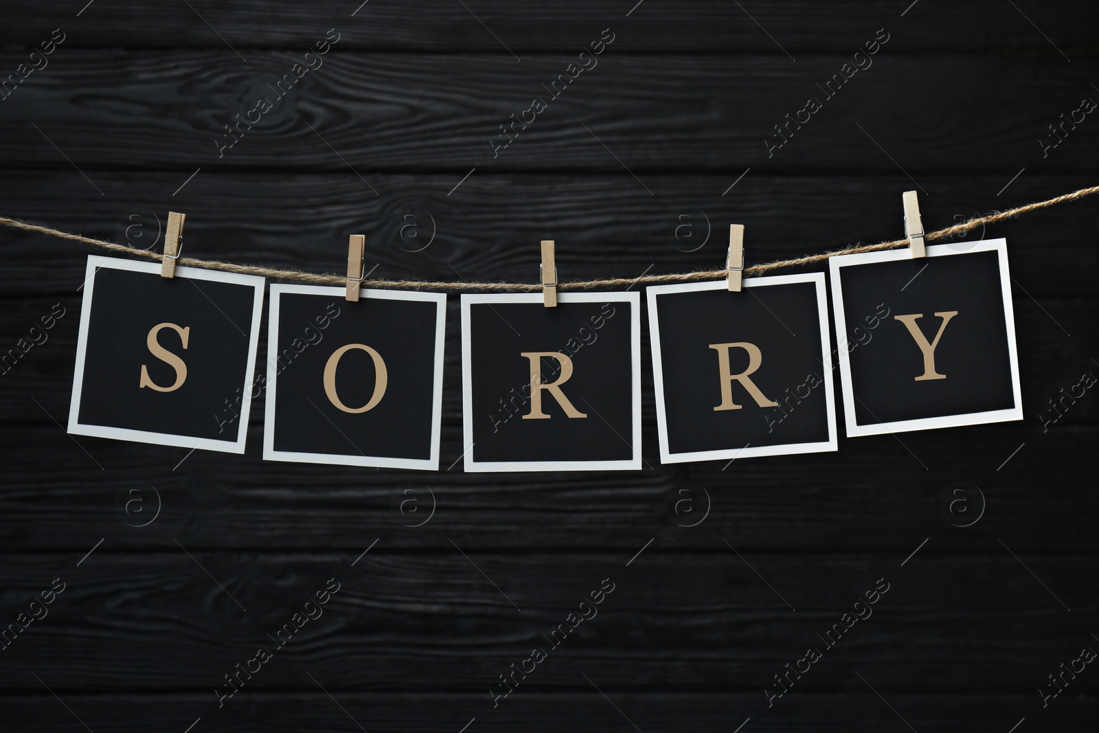 Image of Word Sorry made of paper notes with letters hanging on rope against black wooden background