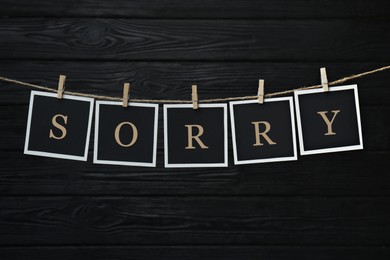 Word Sorry made of paper notes with letters hanging on rope against black wooden background