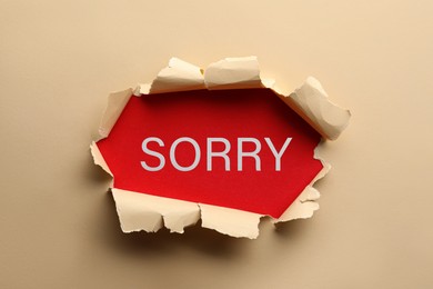 Word Sorry on red background, view through torn beige paper