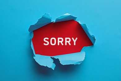 Image of Word Sorry on black background, view through torn light blue paper