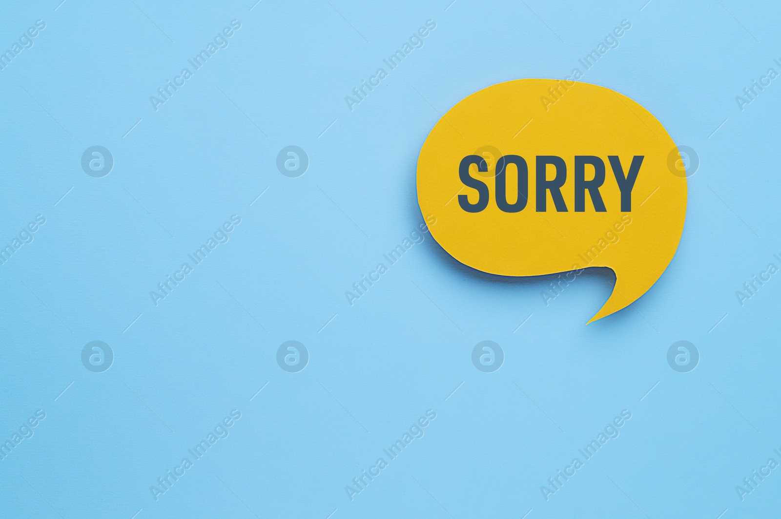 Image of Yellow paper speech balloon with word Sorry on light blue background