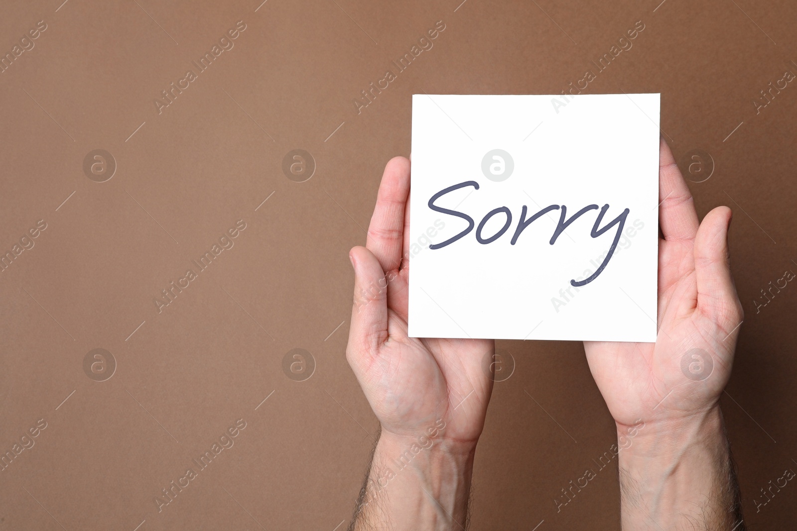 Image of Man holding sheet of paper with word Sorry on brown background, closeup