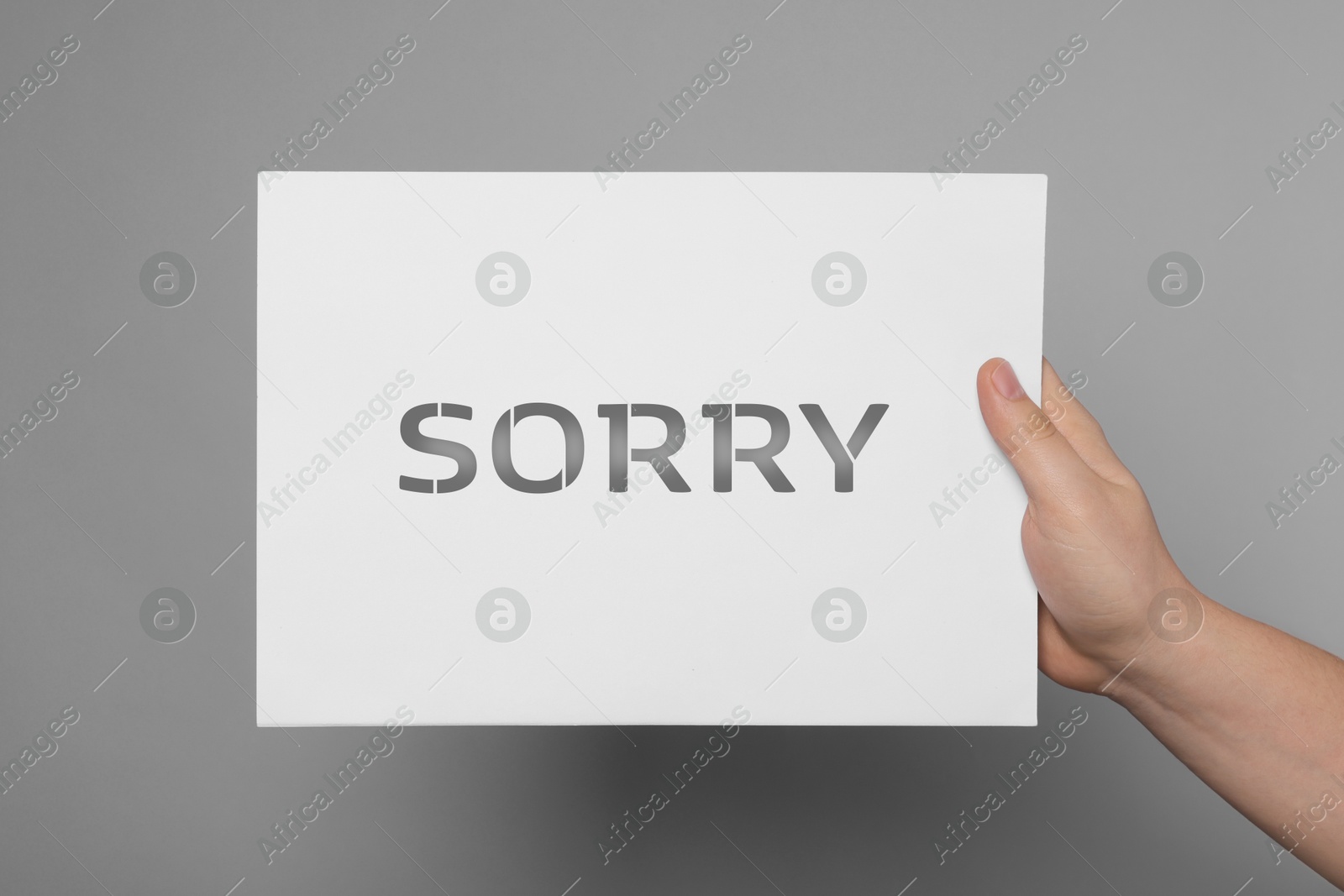 Image of Woman holding sheet of paper with word Sorry on grey background, closeup