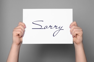 Image of Woman holding sheet of paper with word Sorry on grey background, closeup