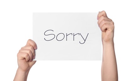 Woman holding sheet of paper with word Sorry on white background, closeup