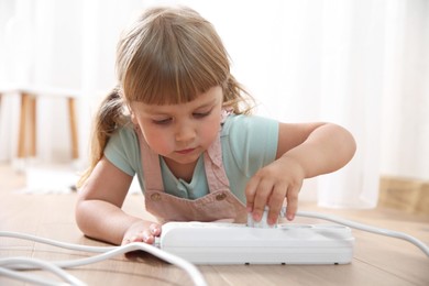 Photo of Little child playing with power strip and plug on floor indoors. Dangerous situation