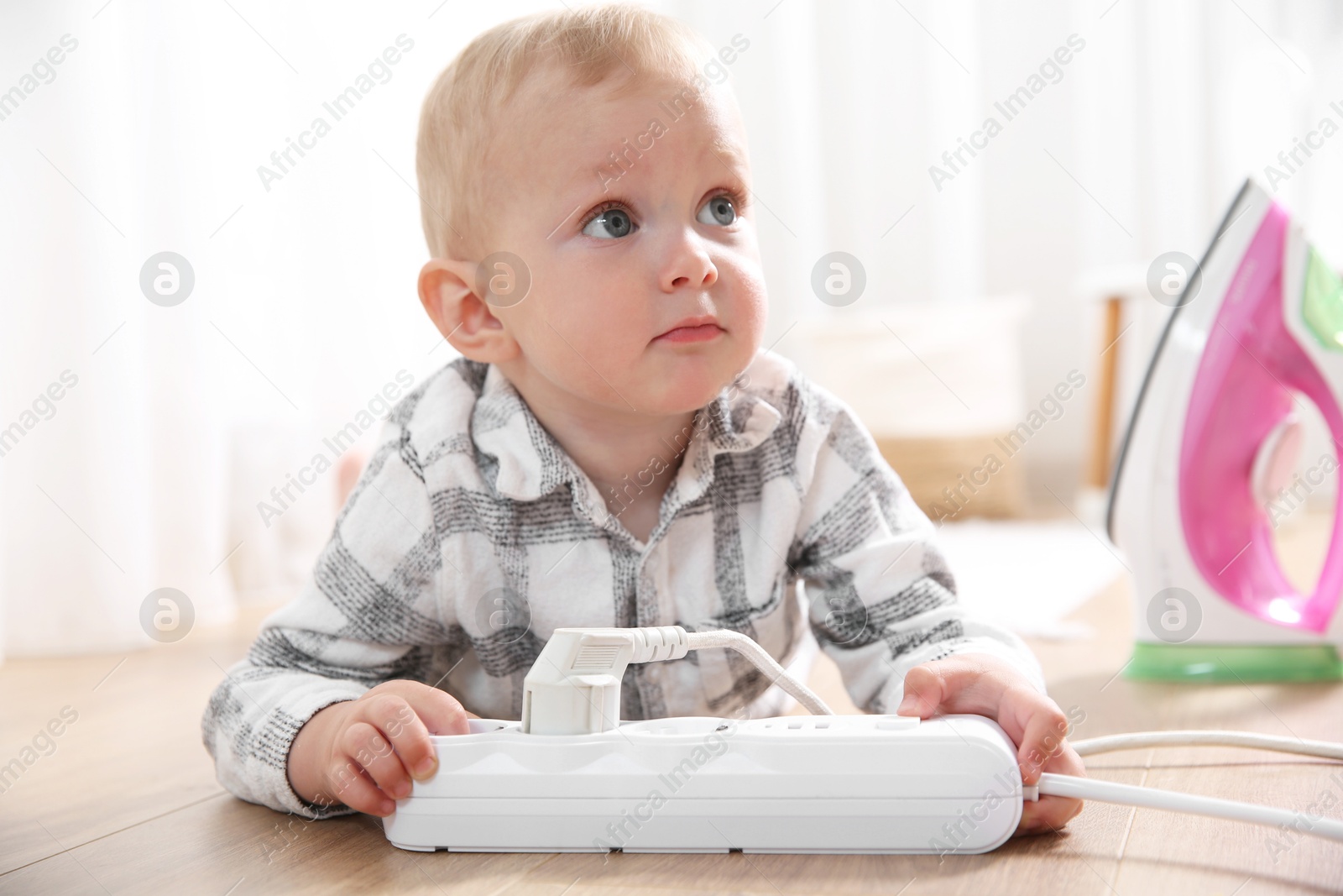 Photo of Little child playing with power strip and iron plug on floor indoors. Dangerous situation