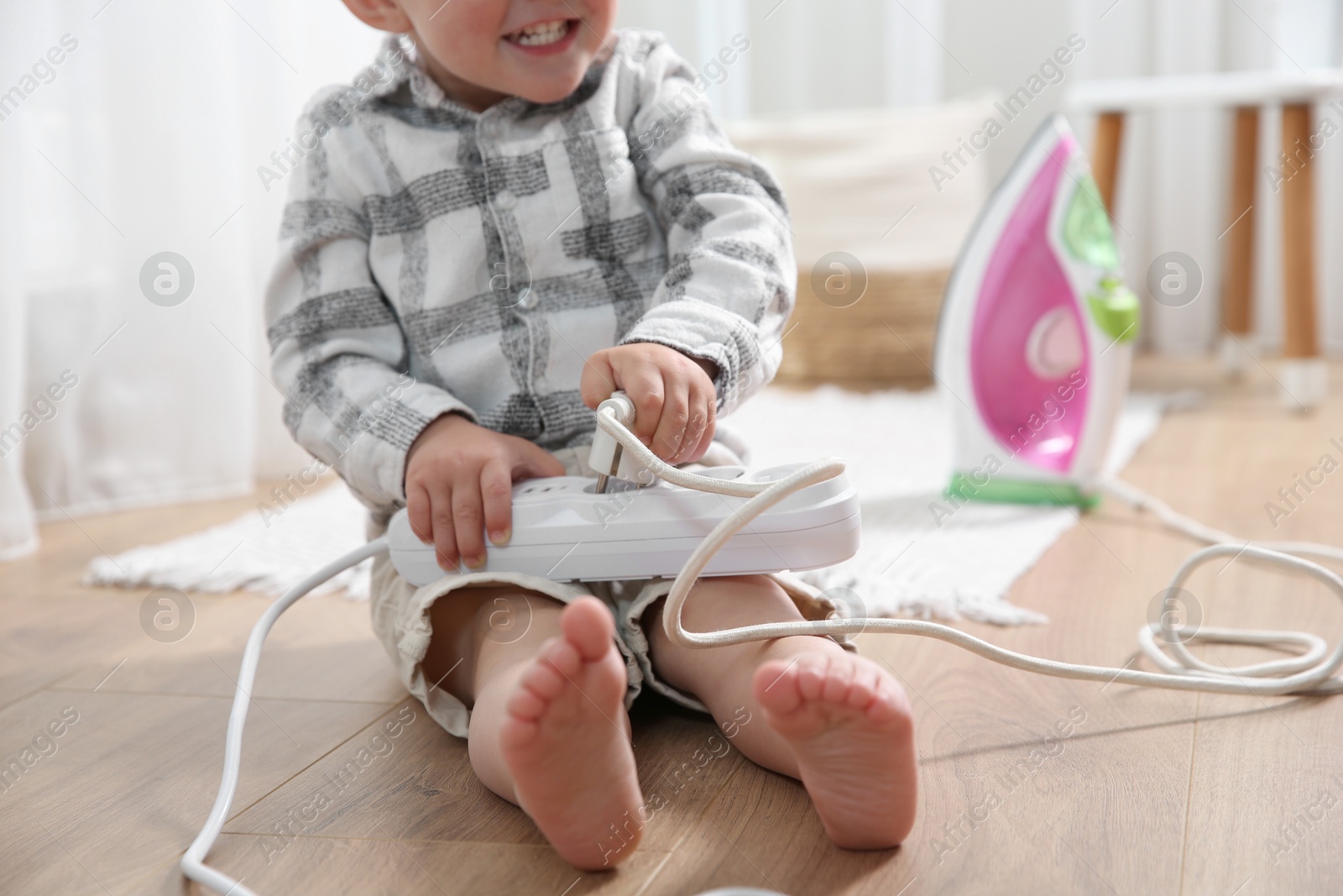Photo of Little child playing with power strip and iron plug on floor at home, closeup. Dangerous situation