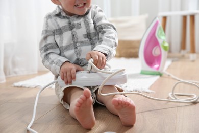 Little child playing with power strip and iron plug on floor at home, closeup. Dangerous situation