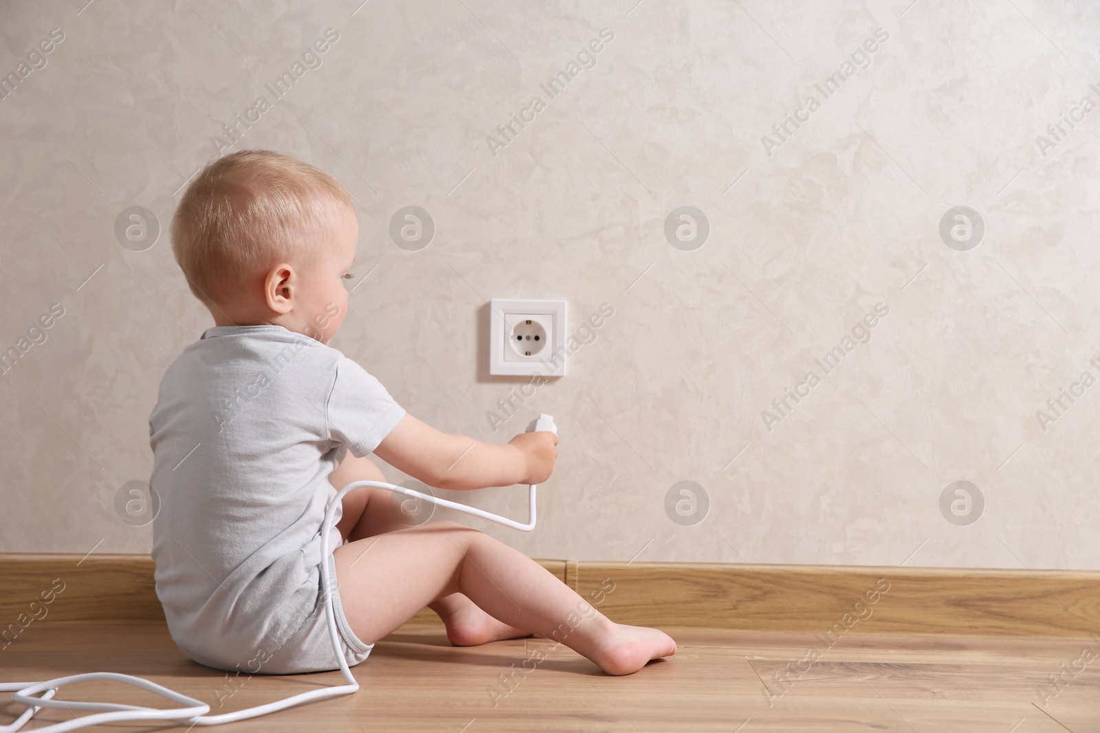 Photo of Little child playing with electrical socket and plug indoors, space for text. Dangerous situation