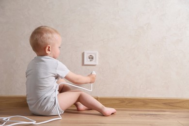 Little child playing with electrical socket and plug indoors, space for text. Dangerous situation