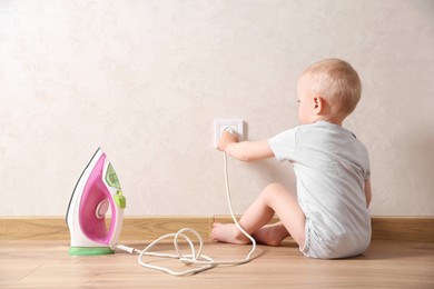 Photo of Little child playing with electrical socket and iron plug indoors. Dangerous situation