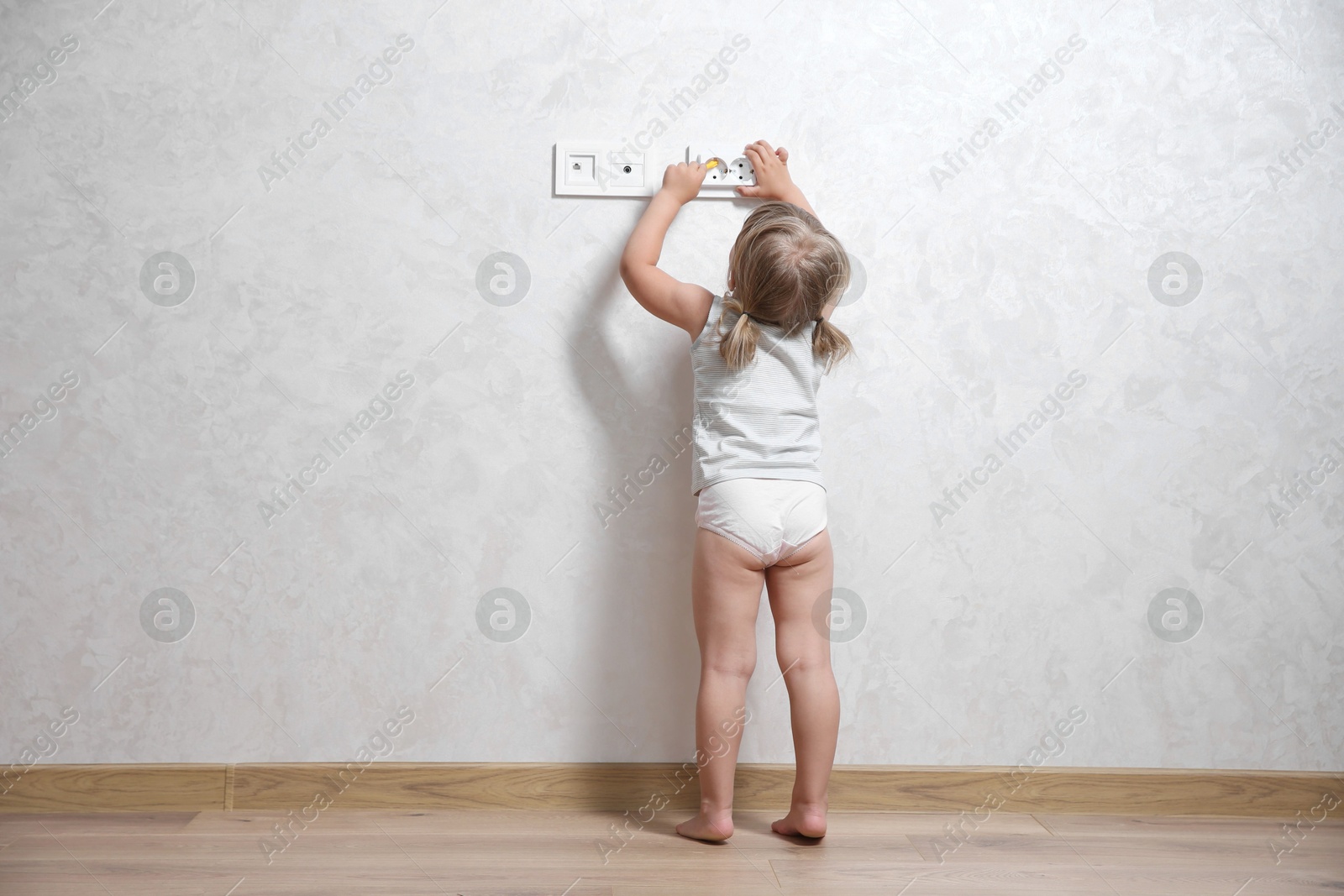 Photo of Little child playing with electrical socket indoors, back view. Dangerous situation