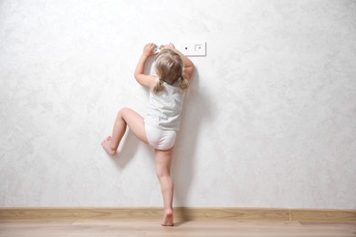 Photo of Little child playing with electrical socket indoors, back view. Dangerous situation