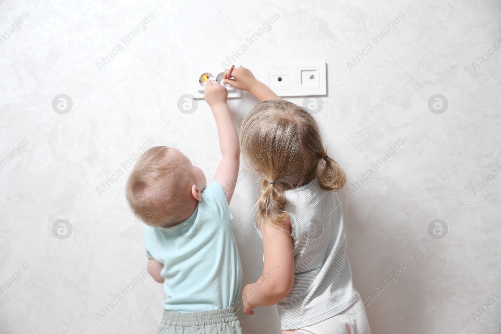 Photo of Little children playing with electrical socket indoors, back view. Dangerous situation