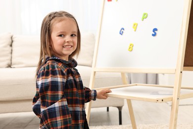 Photo of Cute little girl putting magnetic letters on board at home. Learning alphabet