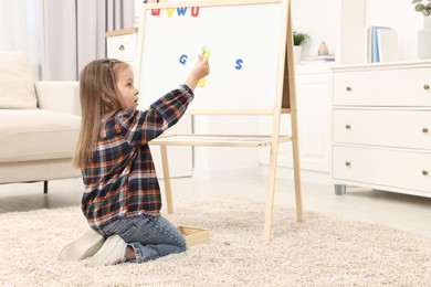 Photo of Cute little girl putting magnetic letters on board at home. Learning alphabet