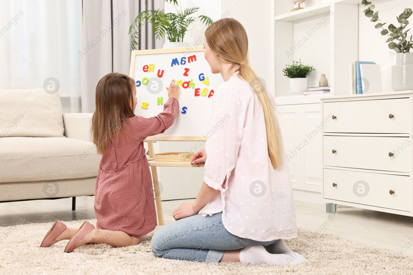 Photo of Mom teaching her daughter alphabet with magnetic letters at home