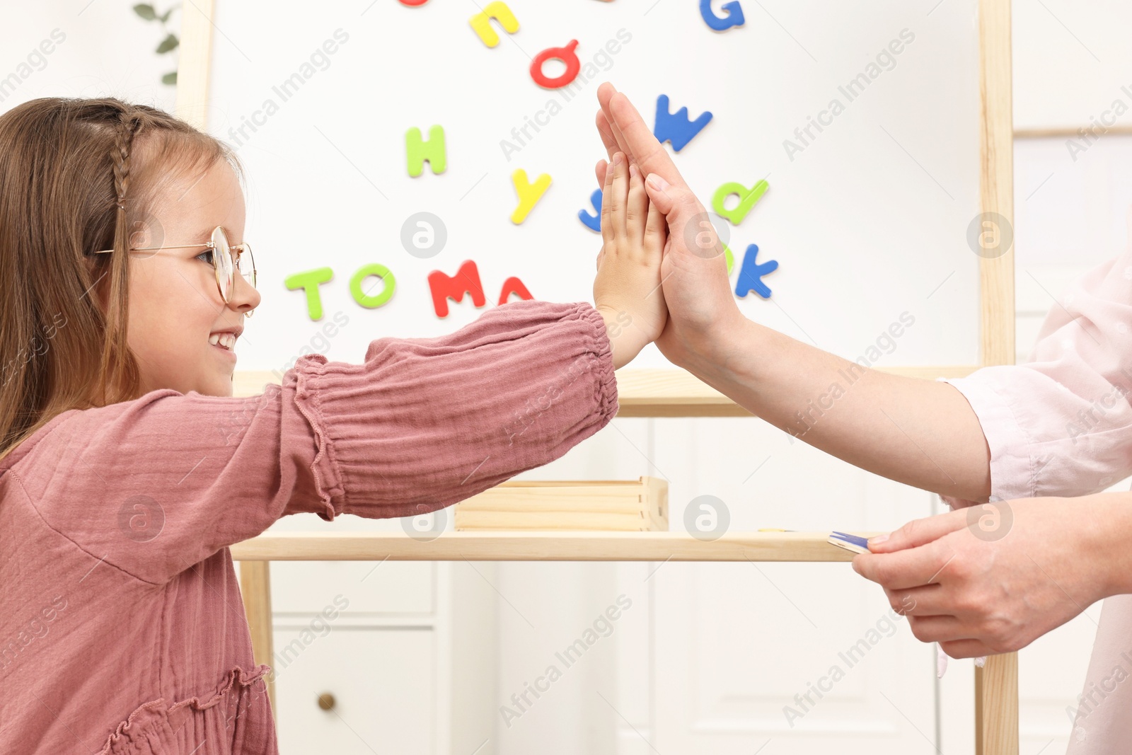 Photo of Mom and daughter giving each other high five while learning alphabet with magnetic letters at home