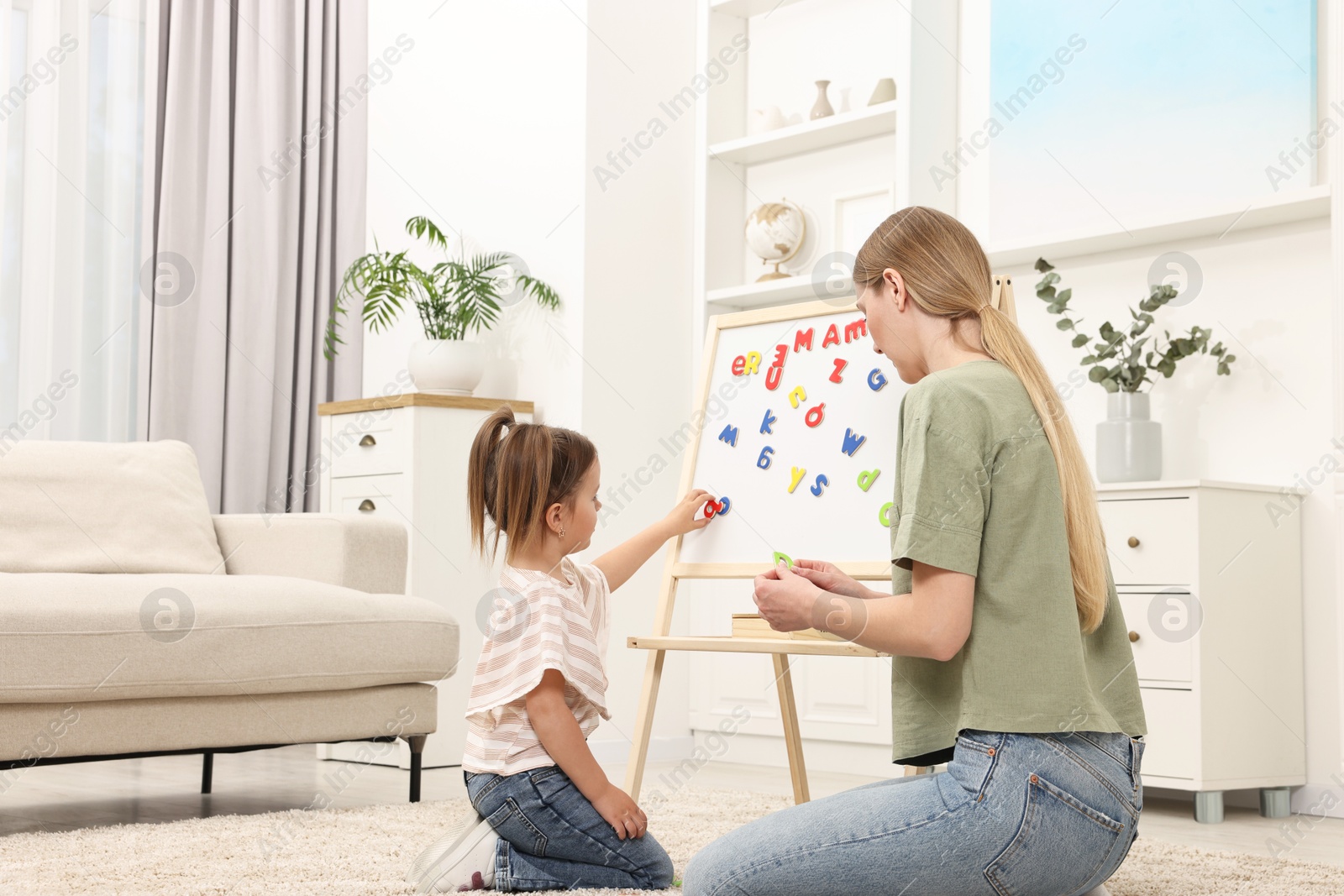 Photo of Mom teaching her daughter alphabet with magnetic letters at home