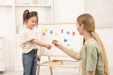 Mom teaching her daughter alphabet with magnetic letters at home