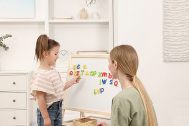 Mom teaching her daughter alphabet with magnetic letters at home