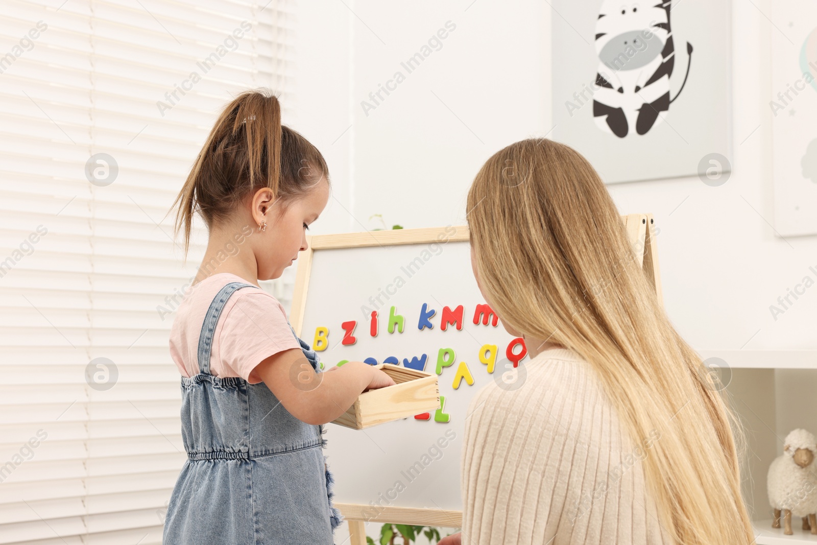 Photo of Mom teaching her daughter alphabet with magnetic letters at home