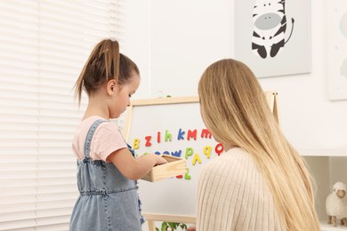 Photo of Mom teaching her daughter alphabet with magnetic letters at home