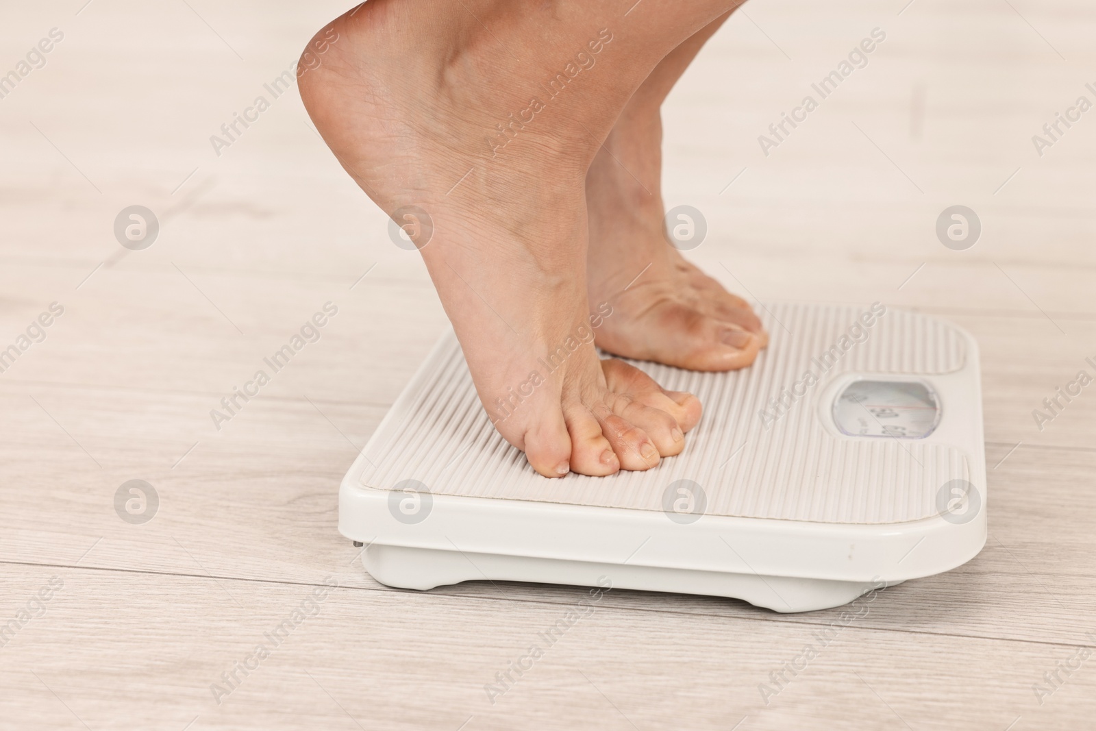 Photo of Woman standing on floor scales indoors, closeup