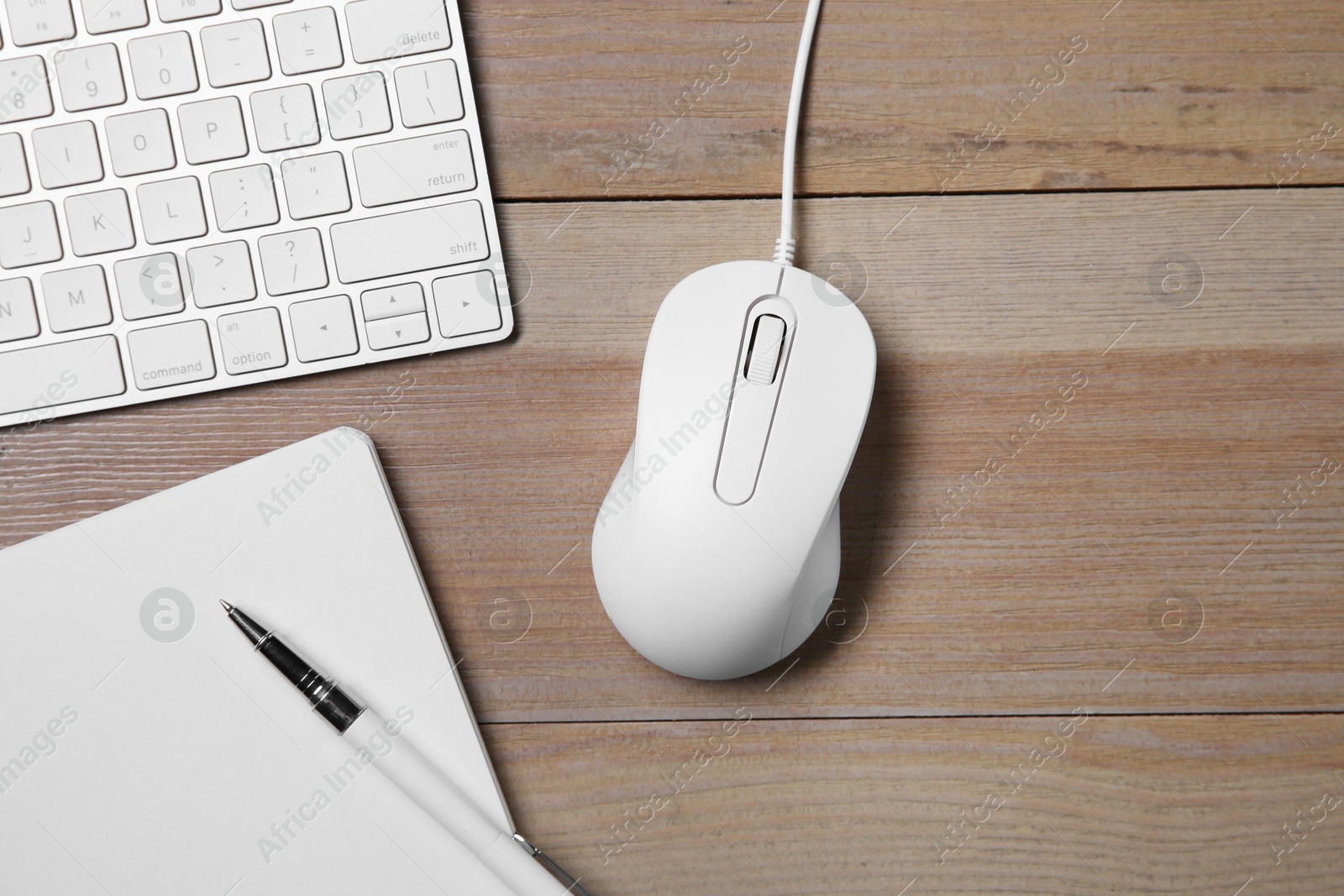 Photo of Wired mouse, notebook, pen and computer keyboard on wooden table, flat lay. Space for text