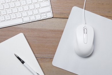 Wired mouse with mousepad, notebook, pen and computer keyboard on wooden table, flat lay