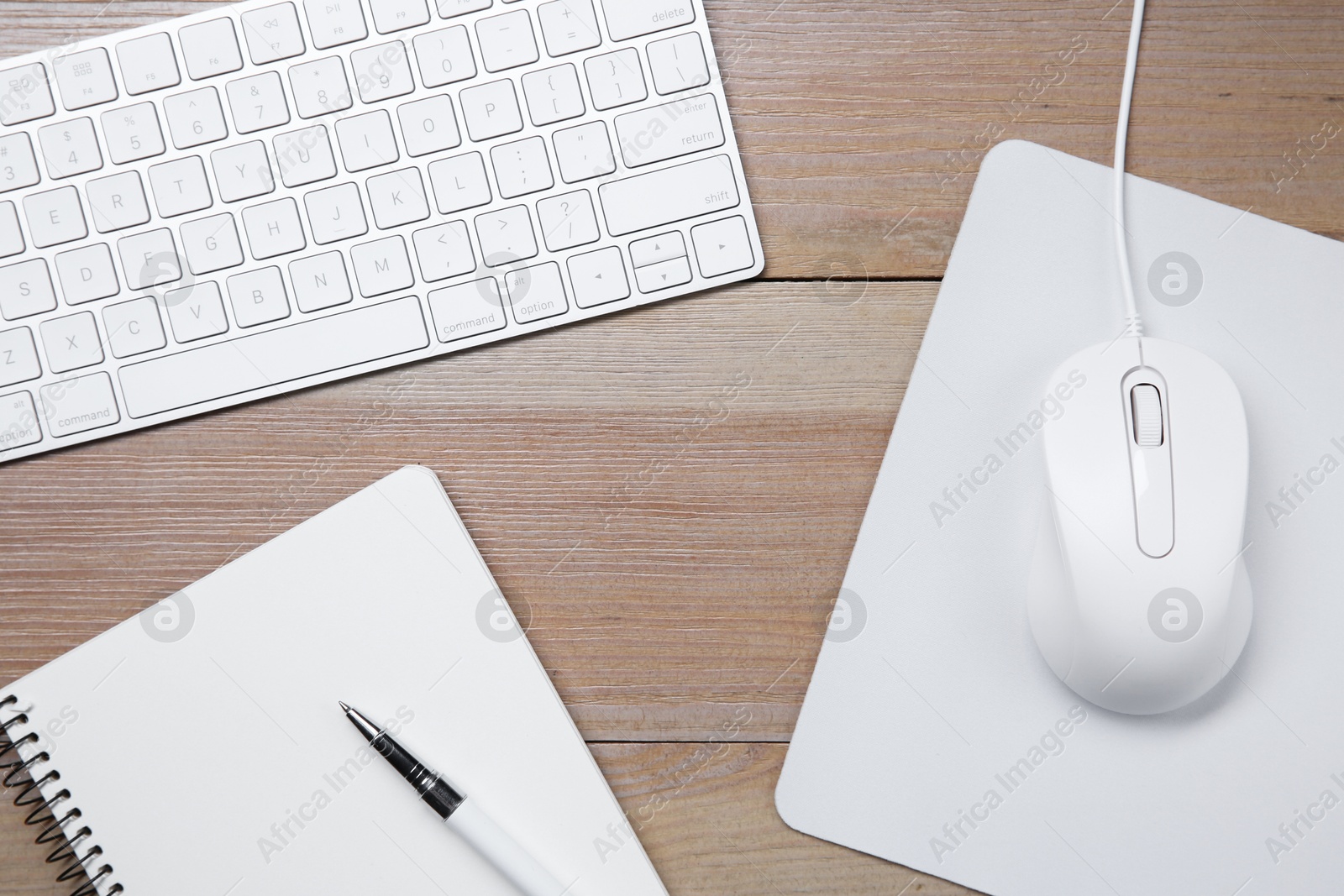 Photo of Wired mouse with mousepad, notebook, pen and computer keyboard on wooden table, flat lay