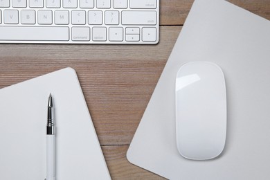 Photo of Wireless mouse with mousepad, notebook, pen and computer keyboard on wooden table, flat lay