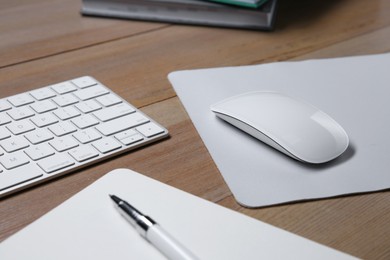 Wireless mouse with mousepad, notebook, pen and computer keyboard on wooden table, closeup