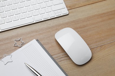 Wireless mouse, notebook, pen and computer keyboard on wooden table, above view