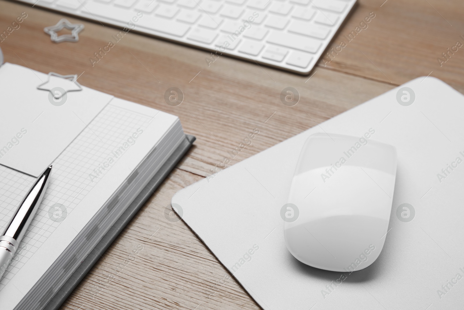 Photo of Wireless mouse, notebook, pen and computer keyboard on wooden table, closeup