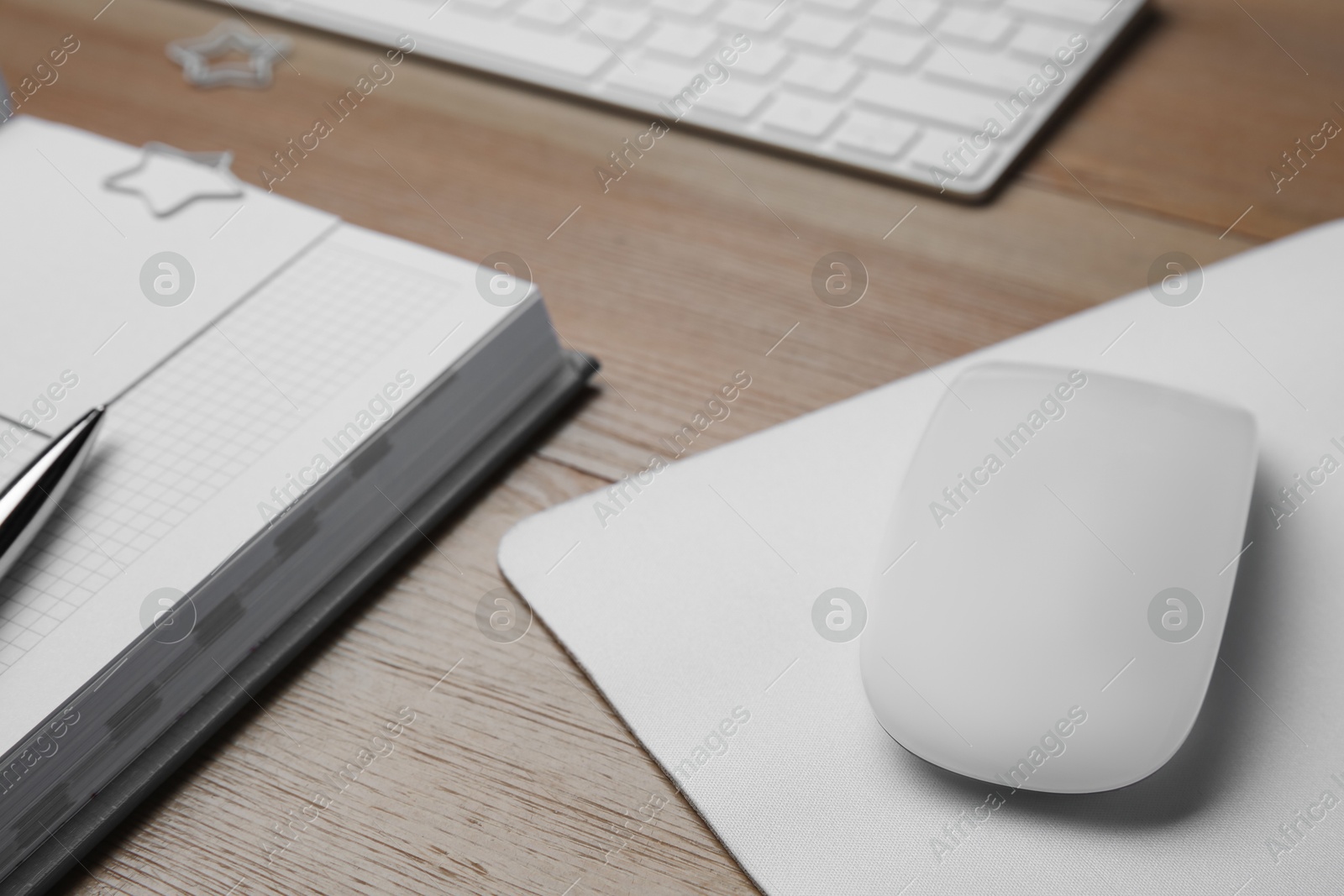 Photo of Wireless mouse, notebook, pen and computer keyboard on wooden table, closeup