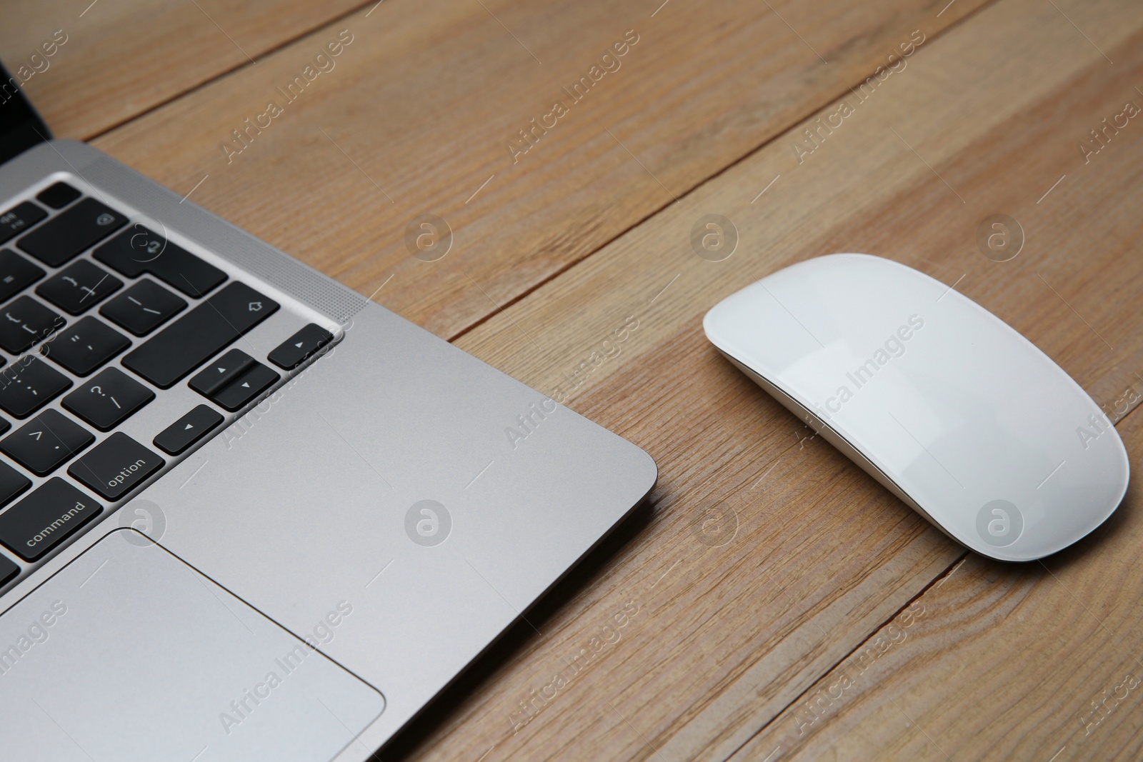 Photo of Wireless mouse and laptop on wooden table, closeup