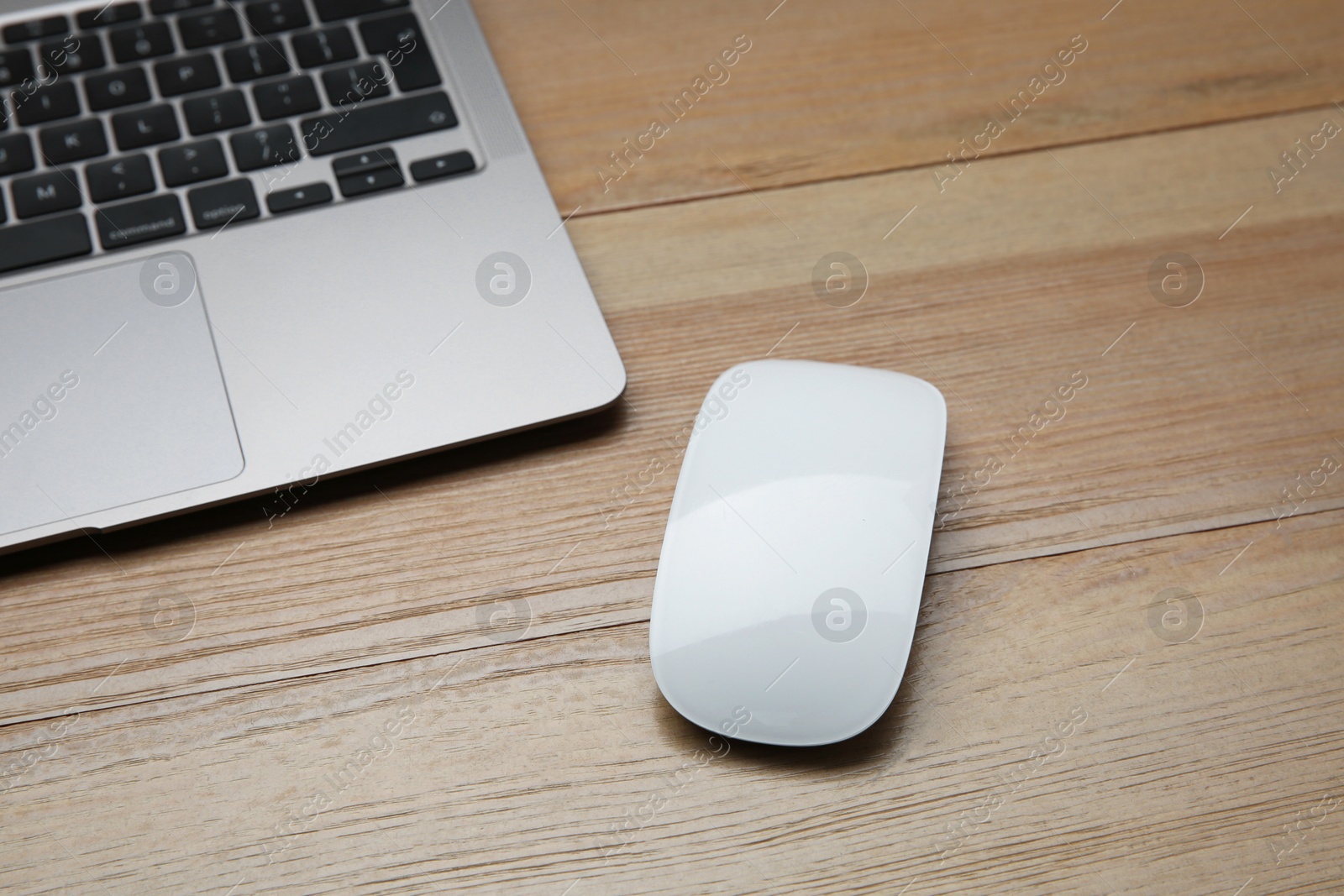 Photo of Wireless mouse and laptop on wooden table, closeup