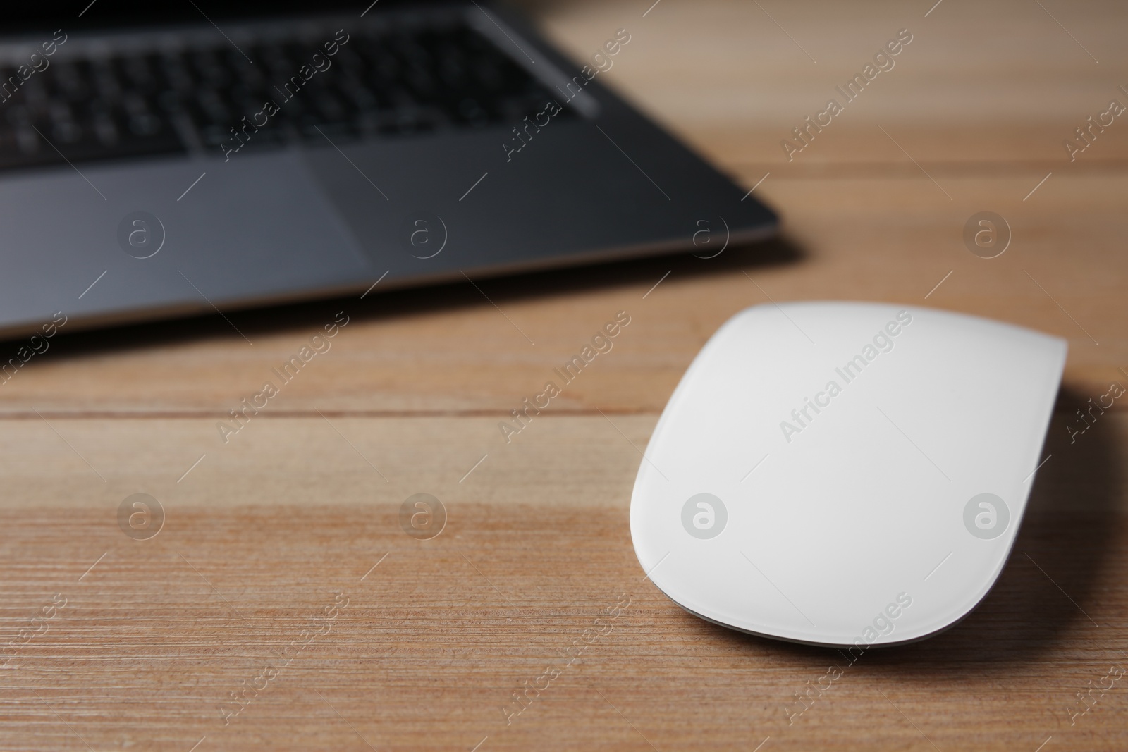 Photo of Wireless mouse and laptop on wooden table, closeup