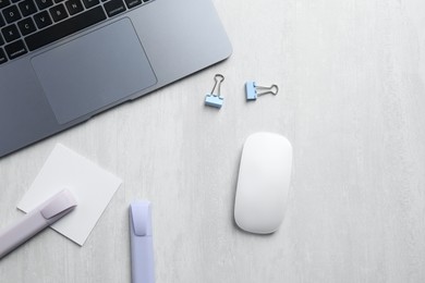 Wireless mouse, stationery and laptop on light wooden table, flat lay