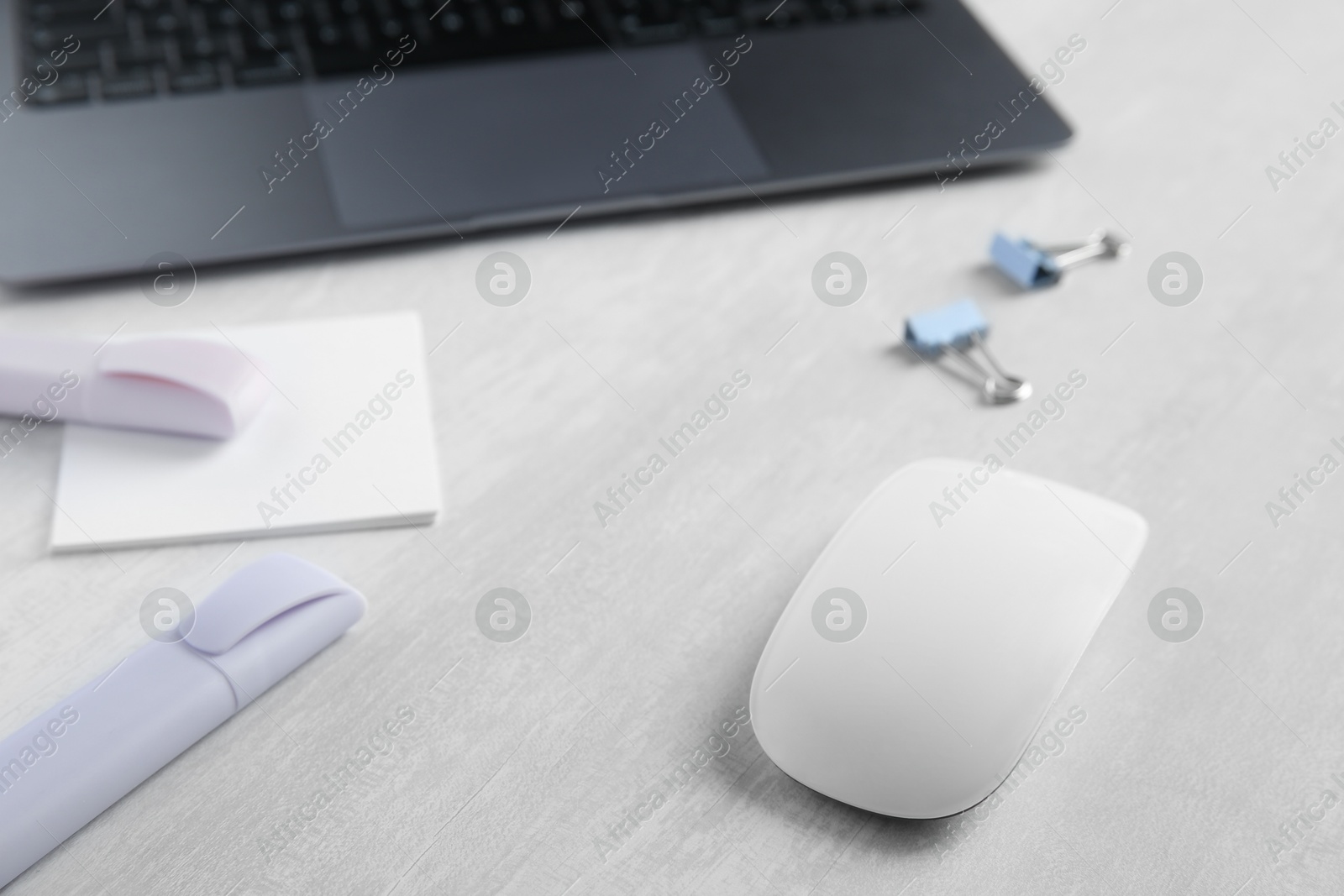 Photo of Wireless mouse and stationery on light wooden table, closeup