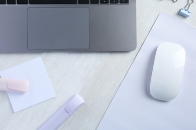 Photo of Wireless mouse with mousepad, stationery and laptop on light wooden table, flat lay