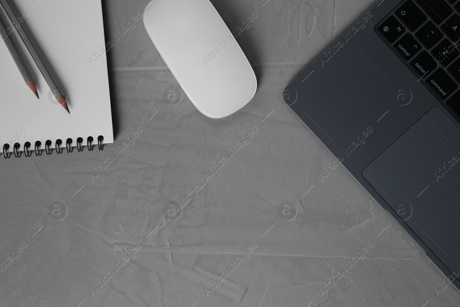 Photo of Wireless mouse, notebook, pencils and laptop on grey textured table, flat lay. Space for text