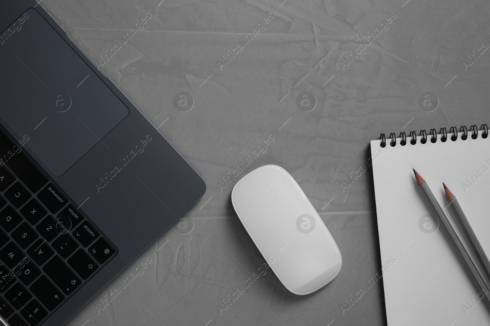 Photo of Wireless mouse, notebook, pencils and laptop on grey textured table, flat lay