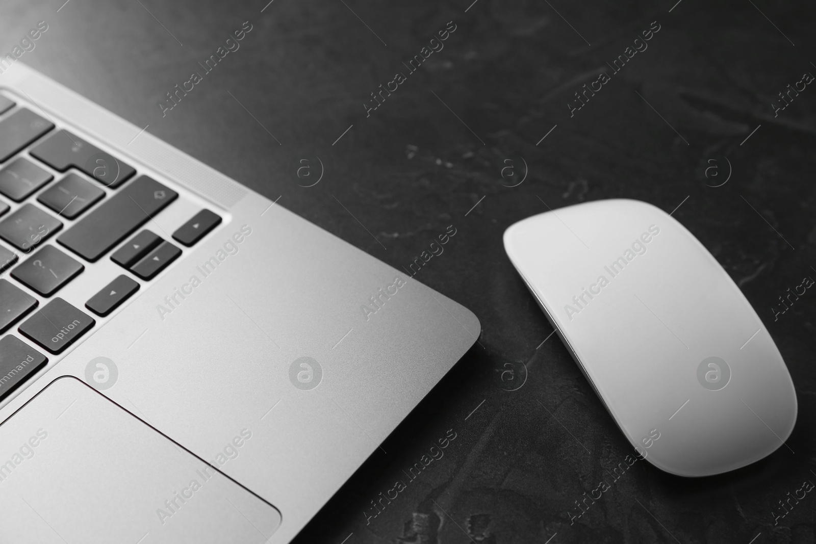 Photo of Wireless mouse and laptop on dark textured table, closeup