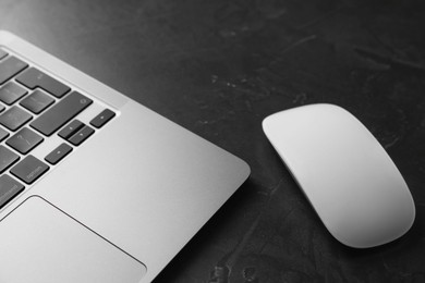 Wireless mouse and laptop on dark textured table, closeup